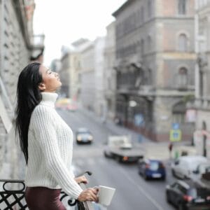 Woman enjoying a moment of relaxation on a balcony overlooking a city street.